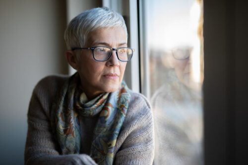 A woman wearing glasses is looking through the window wondering about her life expectancy with heart disease and diabetes.
