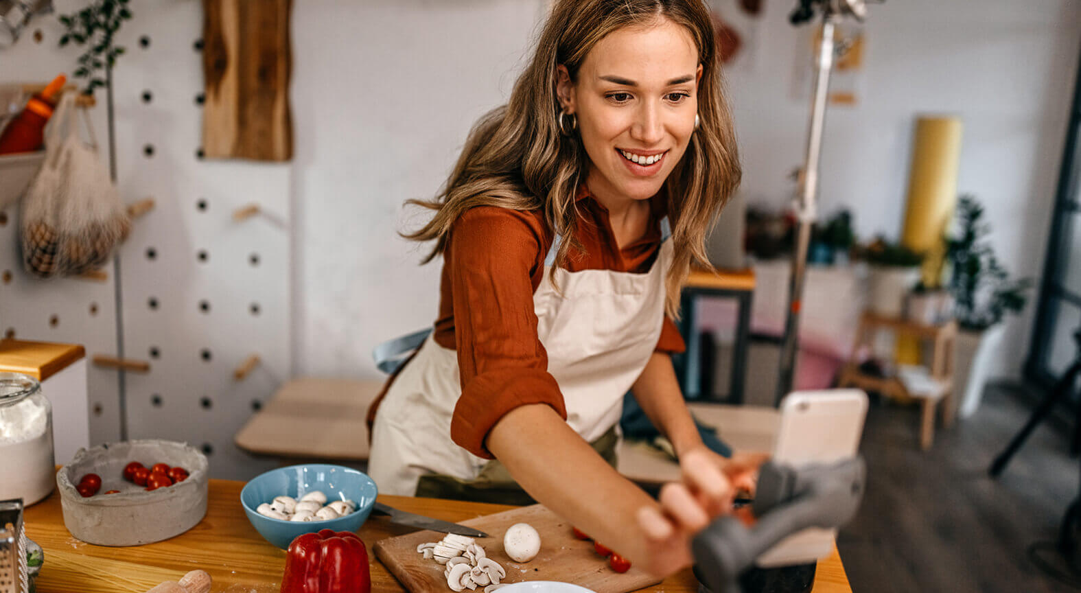 Image of woman cutting vegetables and adjusting phone?>